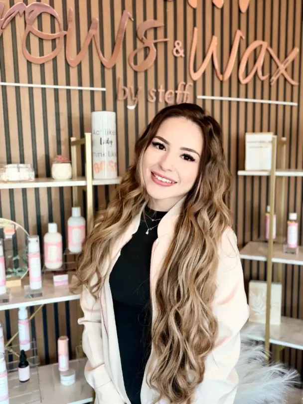 Stylist at Beauty and Brows by Steff, Kennesaw, in front of the studio's branded wall and retail shelving
