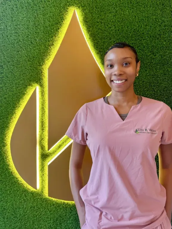 Staff member at Uni K Wax Studio, Brickell, in front of the branded leaf-logo wall