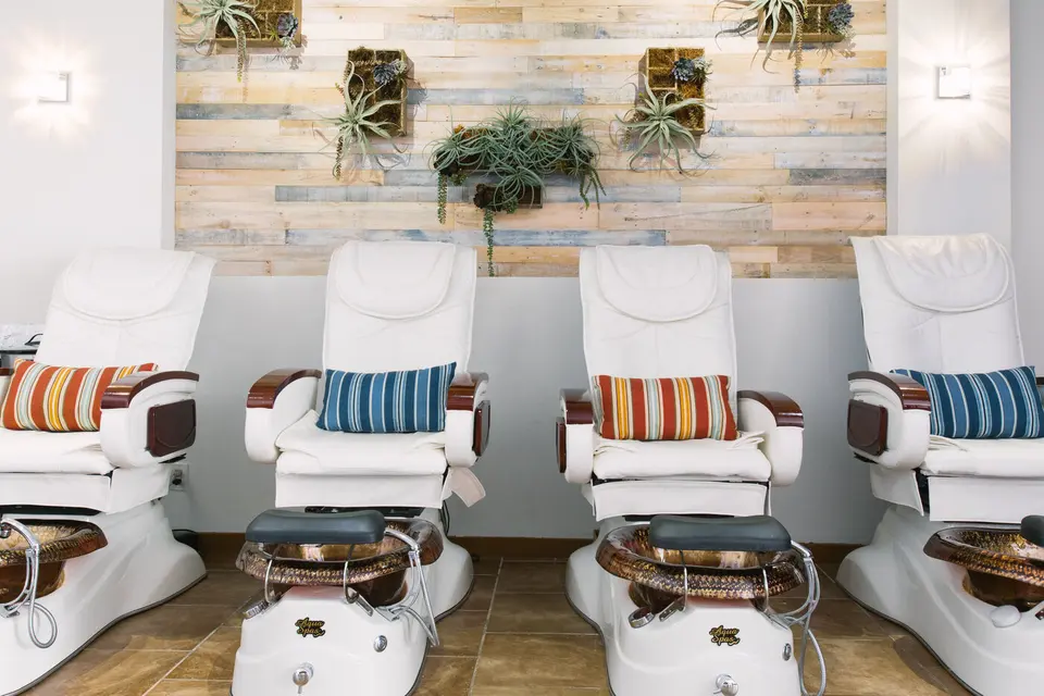 White pedicure chairs and foot baths beneath wood paneling and wall-mounted plants at Venice Soleil